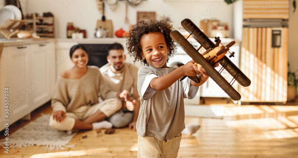 happy multi ethnic family: little son laughing and playing with a toy airplane in front of parents  