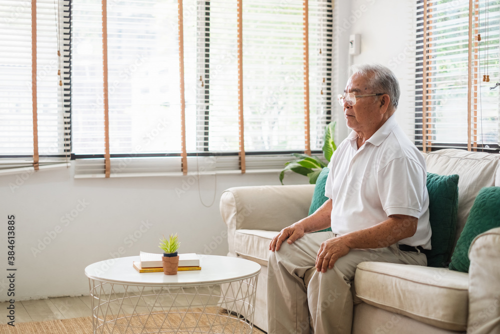 Senior old Asian man sitting on sofa practicing yoga and meditation at home, retirement and wellbein