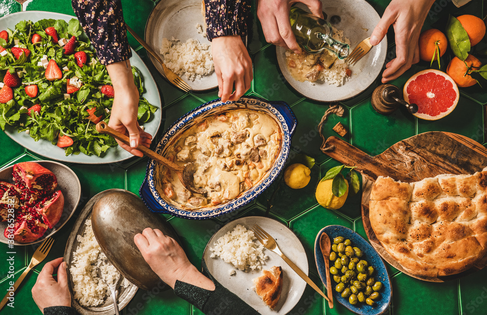 Family having Turkish dinner. Flat-lay of people hands serving and eating with lamb in yogurt sauce,