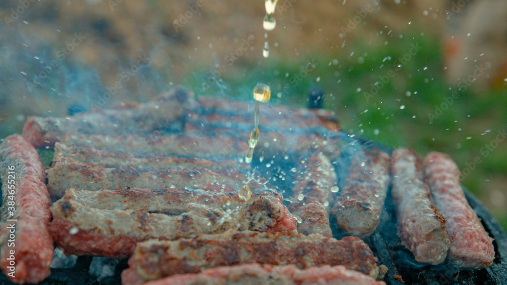 CLOSE UP: Person cooking meatrolls on the grill splashes them with cold beer.