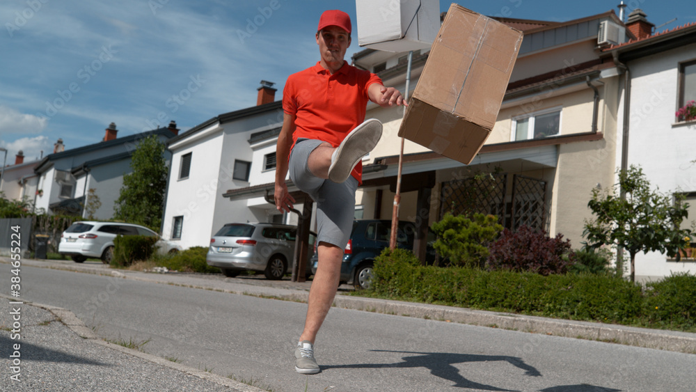 LOW ANGLE: Careless young courier kicking customers orders at their doorsteps.