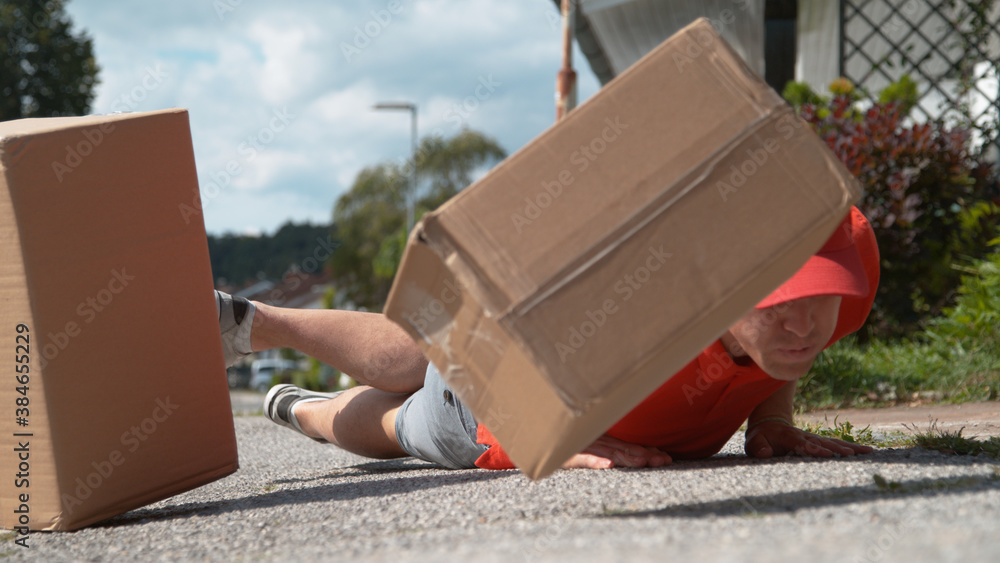 CLOSE UP: Uncoordinated delivery man falls to ground and drops cardboard boxes