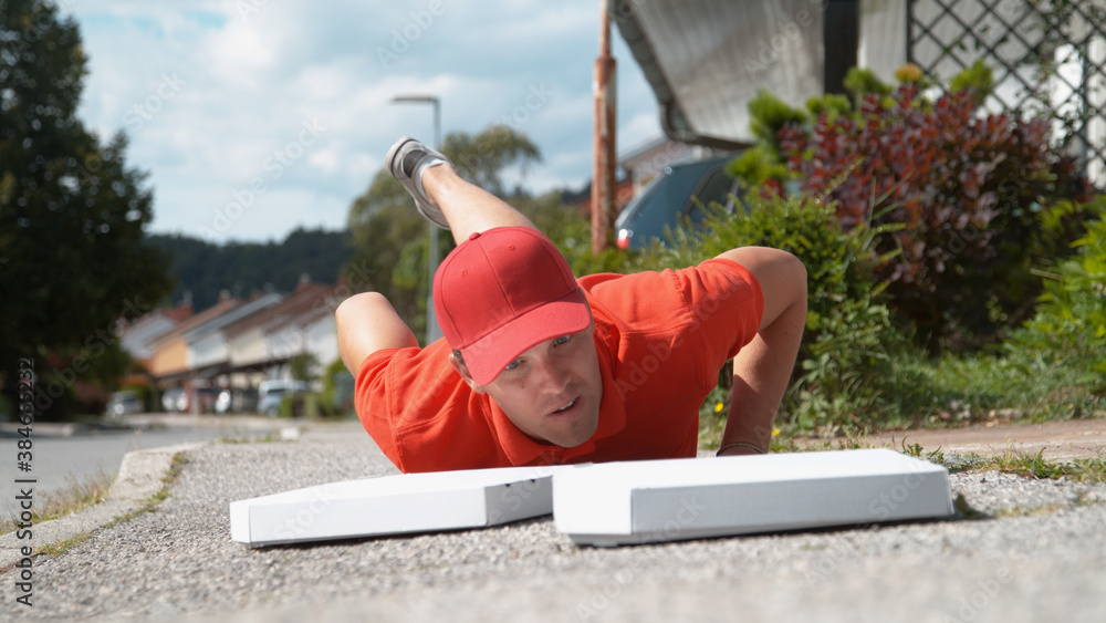 CLOSE UP: Uncoordinated delivery man falls to the ground and drops two pizzas.