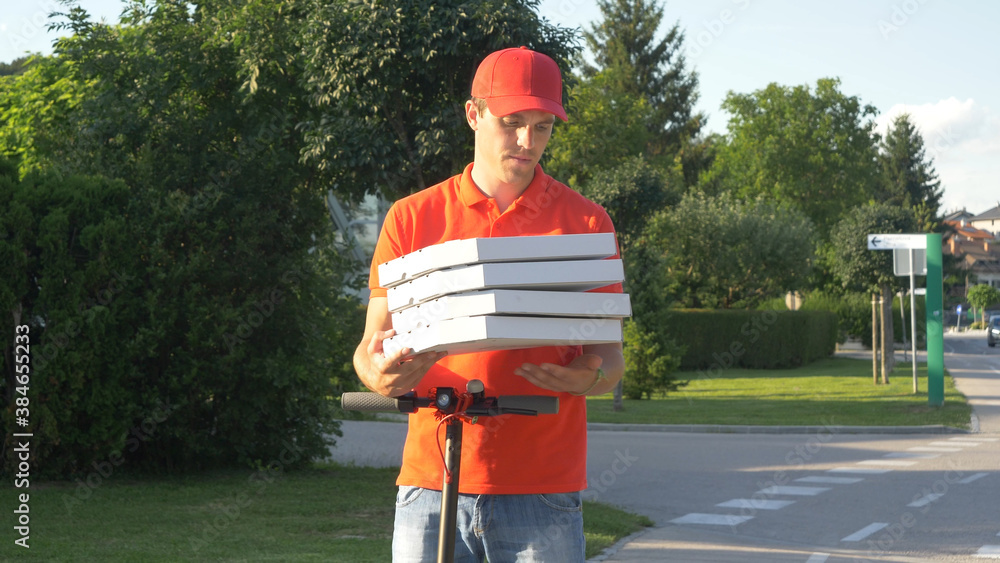 CLOSE UP: Young courier holds pizza boxes before delivering them on e-scooter