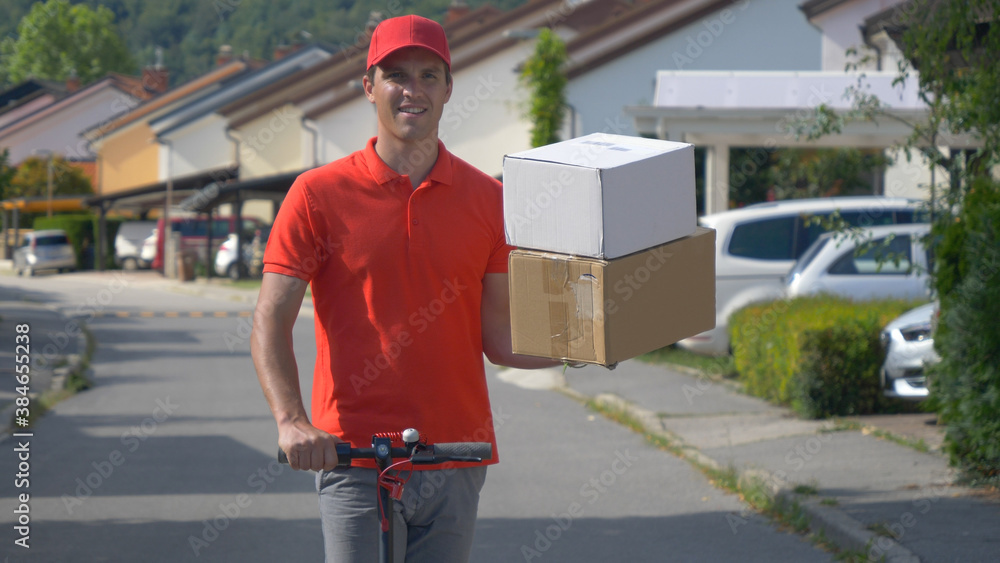 CLOSE UP Content young courier rides e-scooter down the street with two packages