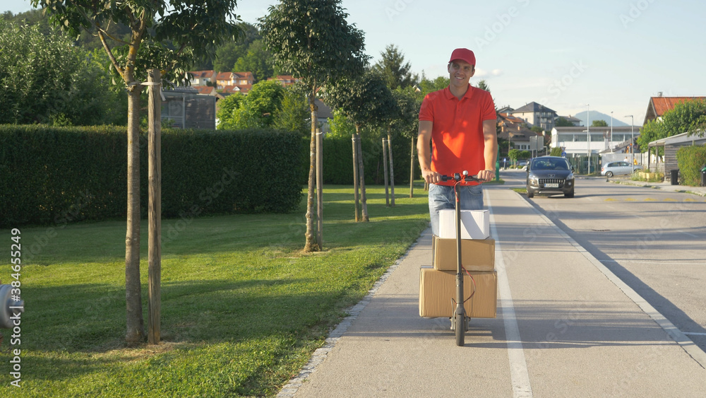 Smiling courier rides an electric scooter while delivering packages in suburbs