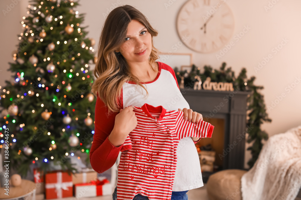 Beautiful pregnant woman with baby clothes at home on Christmas eve