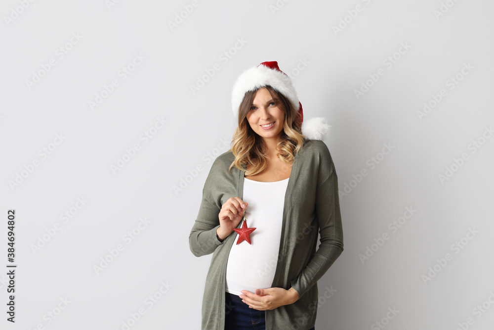 Beautiful pregnant woman with Christmas tree decoration on light background