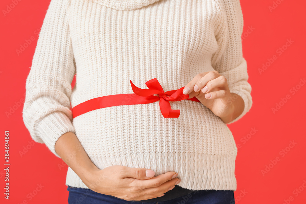 Beautiful pregnant woman with ribbon around her waist on color background