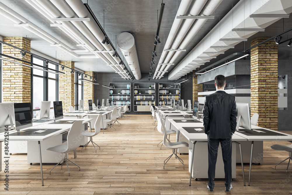 Businessman standing in loft style office with computers