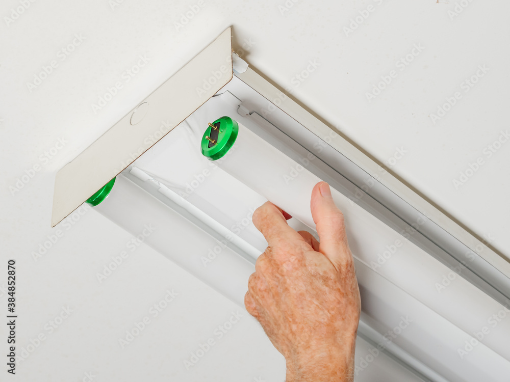 Electrician changing fluorescent light bulb in ceiling light fixture. Man replacing burned out fluor