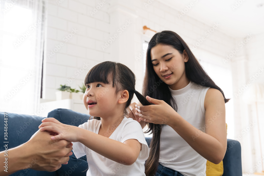 Beautiful Asian young mother is making hairstyle to her cute daughter. Happy family enjoy spending a