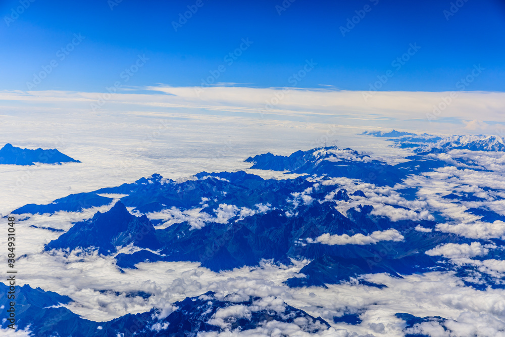 Aerial view above the clouds and mountain peaks on a sunny day.