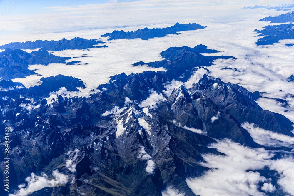 Aerial view above the clouds and mountain peaks on a sunny day.