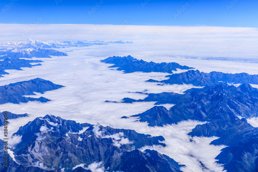 Aerial view above the clouds and mountain peaks on a sunny day.