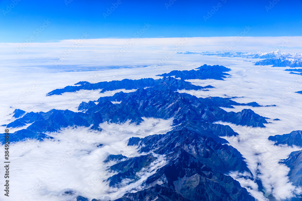 Aerial view above the clouds and mountain peaks on a sunny day.