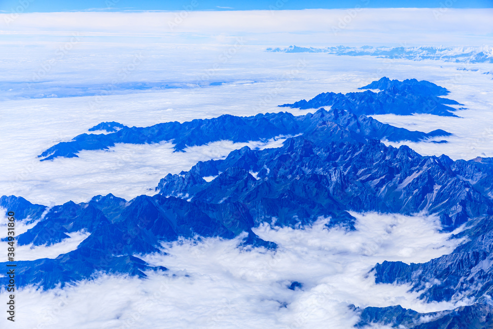 Aerial view above the clouds and mountain peaks on a sunny day.