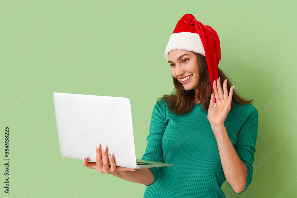 Beautiful young woman in Santa hat and with laptop on color background