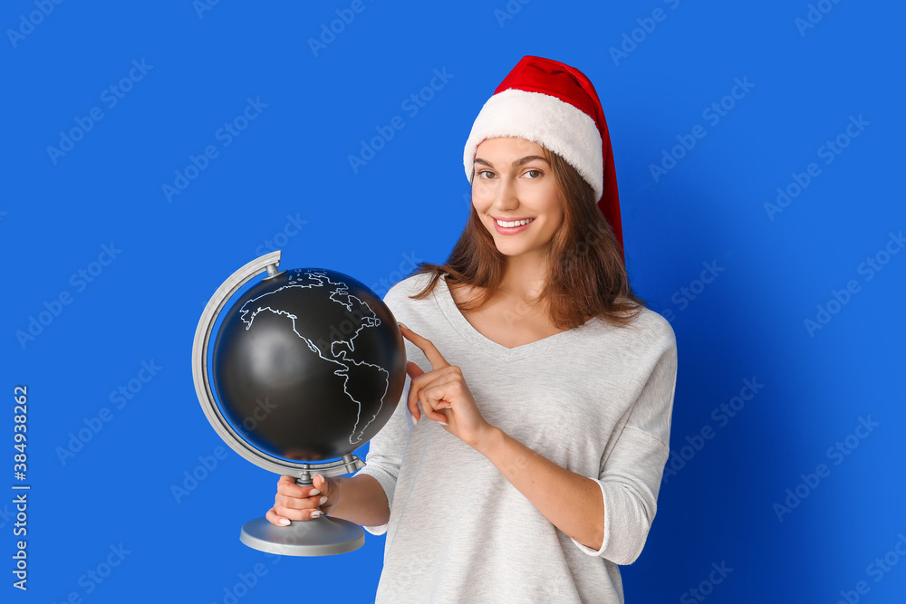 Beautiful young woman in Santa hat and with globe on color background. Christmas holidays concept