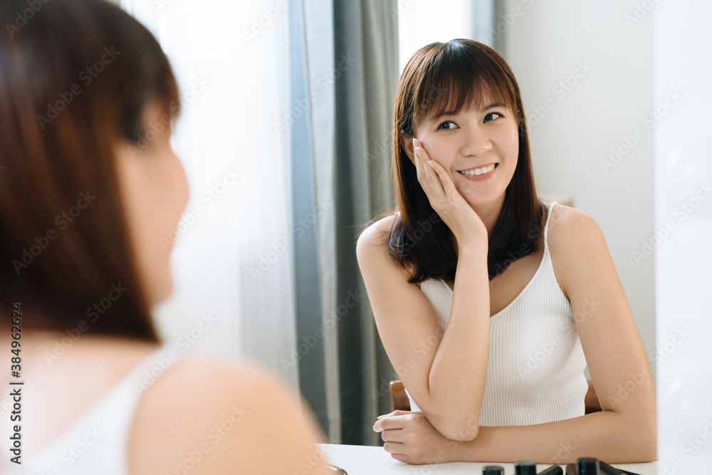 beautiful japanese girl is looking at her reflection in front of mirror with pleasant expression. yo