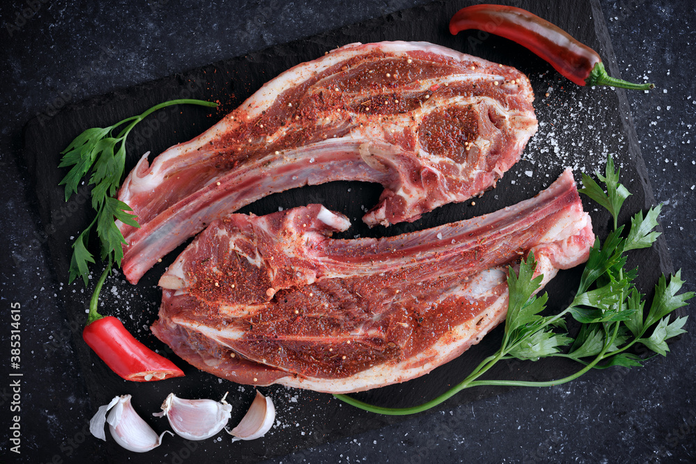 Raw meat. Lamb steaks with spices on the cutting Board. On a black stone background.