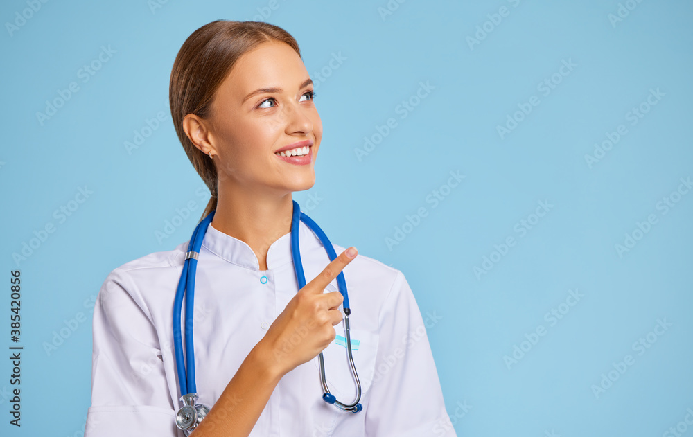 friendly doctor nurse in  uniform smiles and pointing at empty space against a blue background.