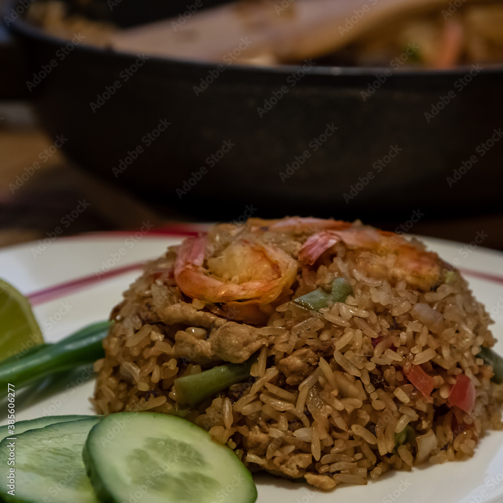 A compact fried rice mound on a white plate with three red shrimps on the top. This is a Thai dish c