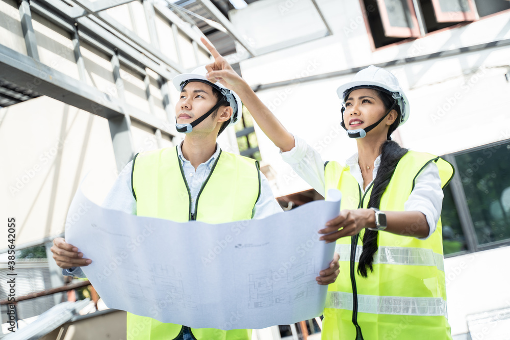 Asian young engineer man and woman look at drawing and discuss.