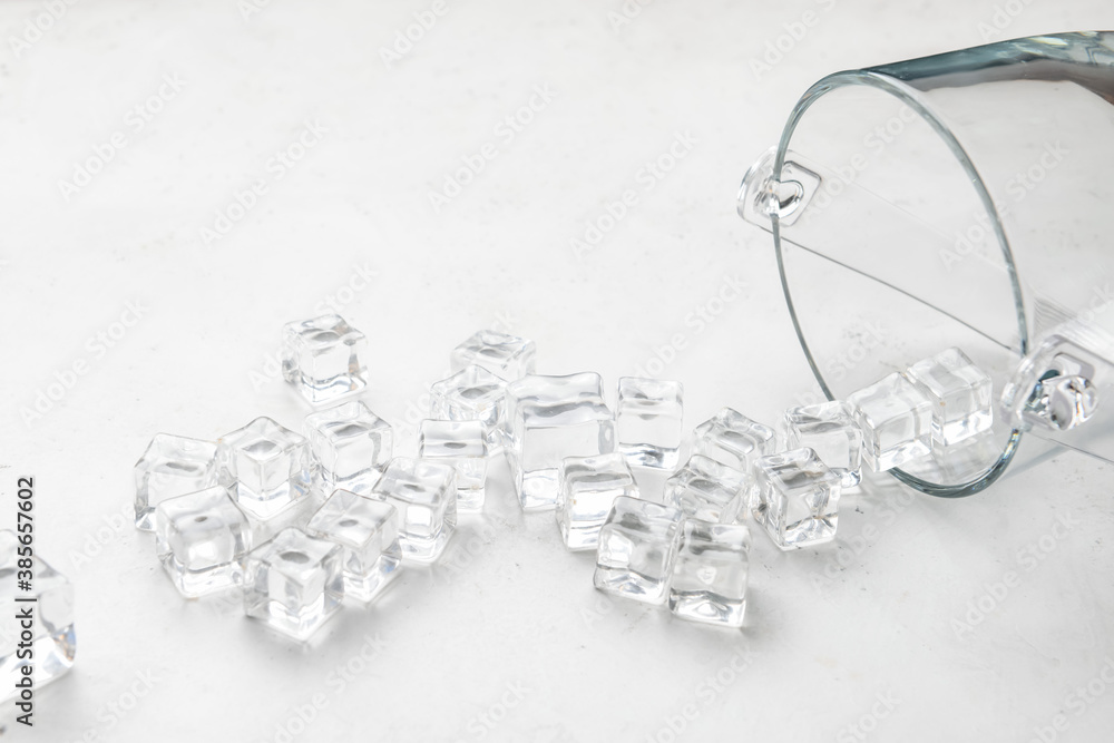 Overturned glass and ice cubes on light background