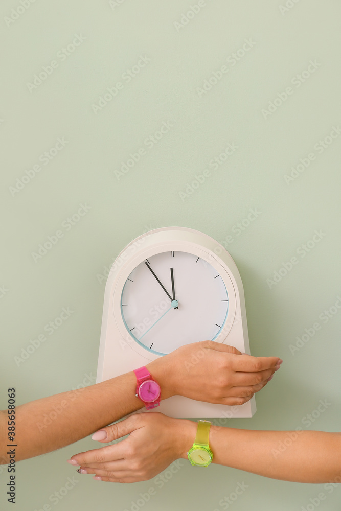 Female hands with watches and clock on color background