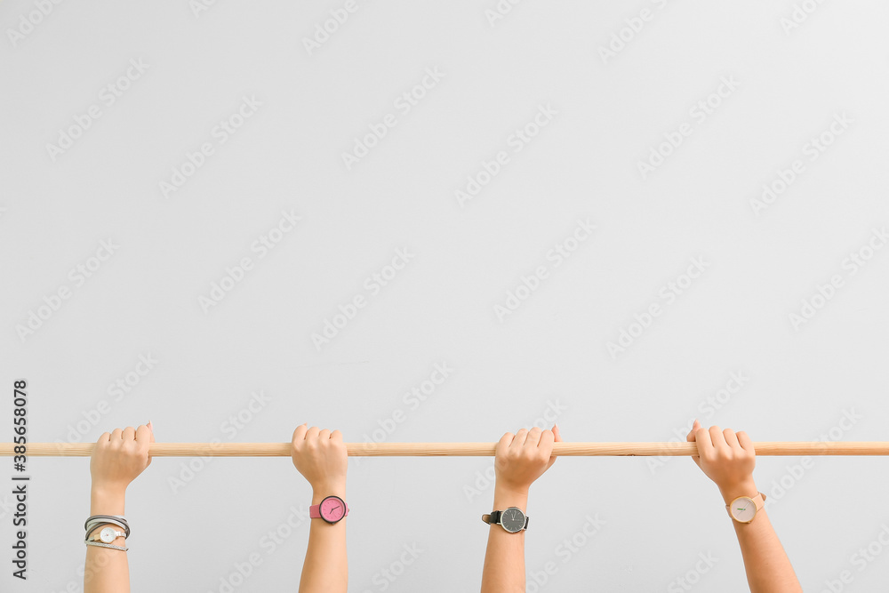 Female hands with watches holding wooden stick on light background