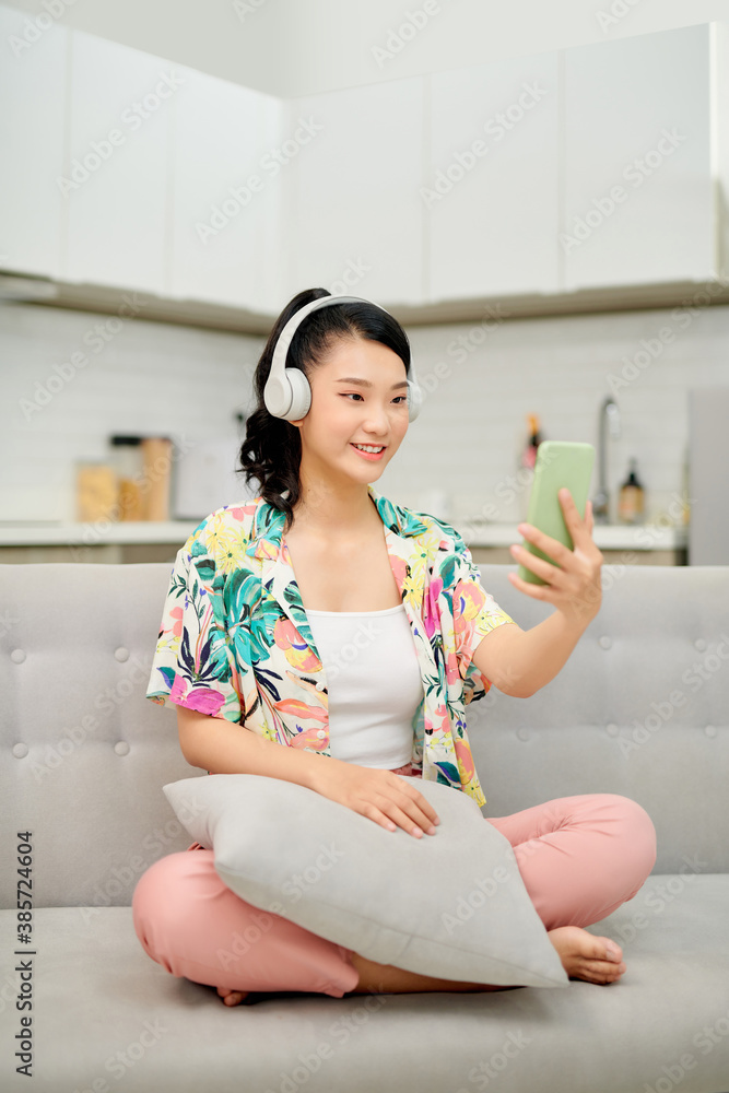 Portrait beautiful young asian woman use smart mobile phone with headphone for listen music on sofa 