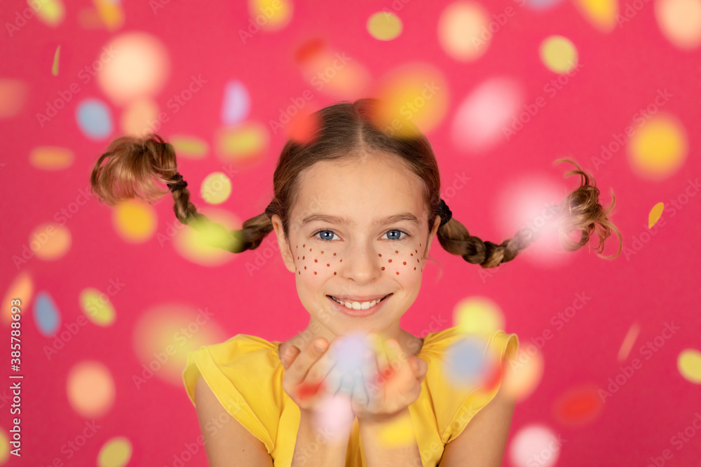 Fancy child with pigtails blowing confetti against pink background