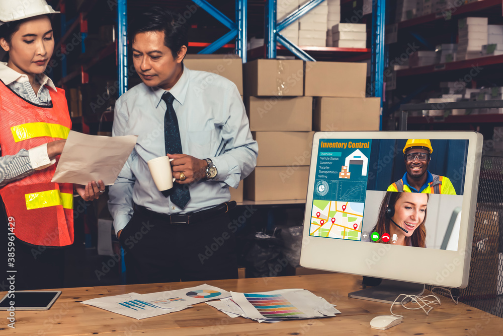 Warehouse staff talking on video call at computer screen in storage warehouse . Online software tech