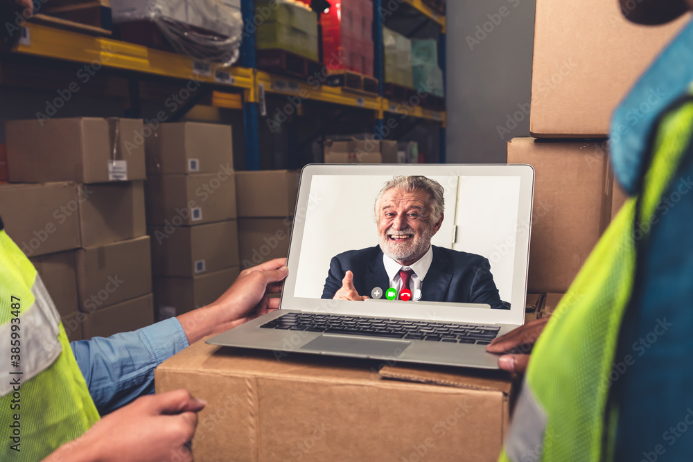 Warehouse staff talking on video call at computer screen in storage warehouse . Online software tech