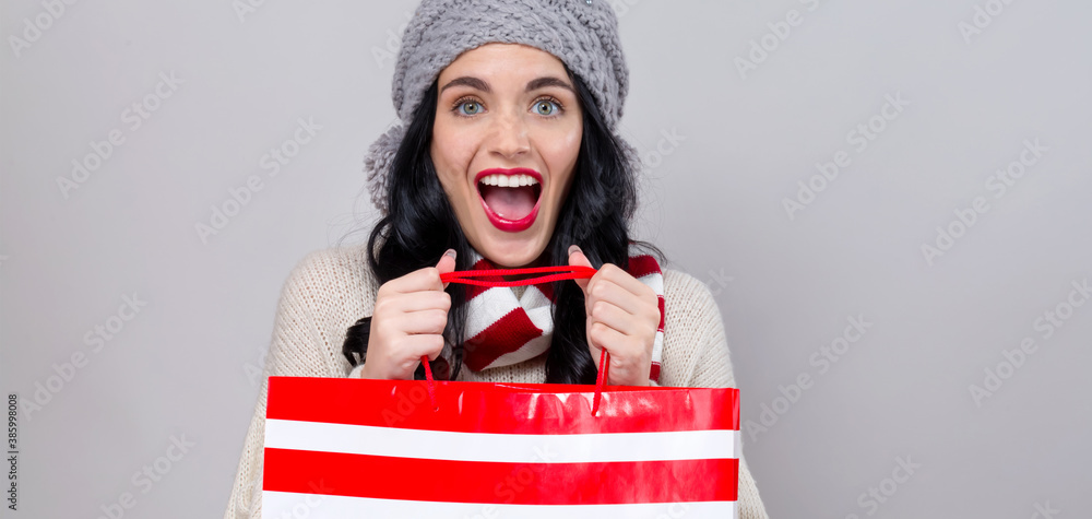 Happy young woman holding a shopping bag on a gray background