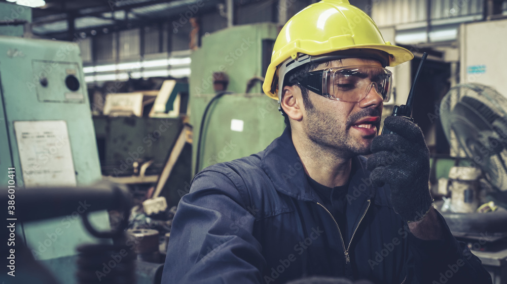 Factory worker talking on portable radio while inspecting machinery parts . Industrial and engineeri