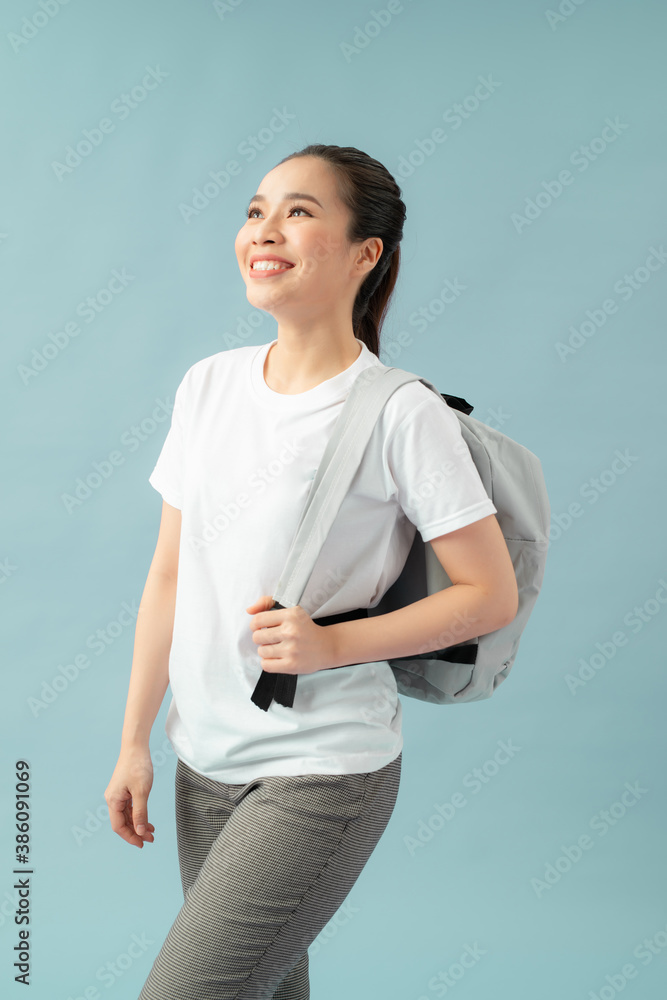 Portrait of energetic teenager girl isolated on blue background pulling forward straps of gray hipst