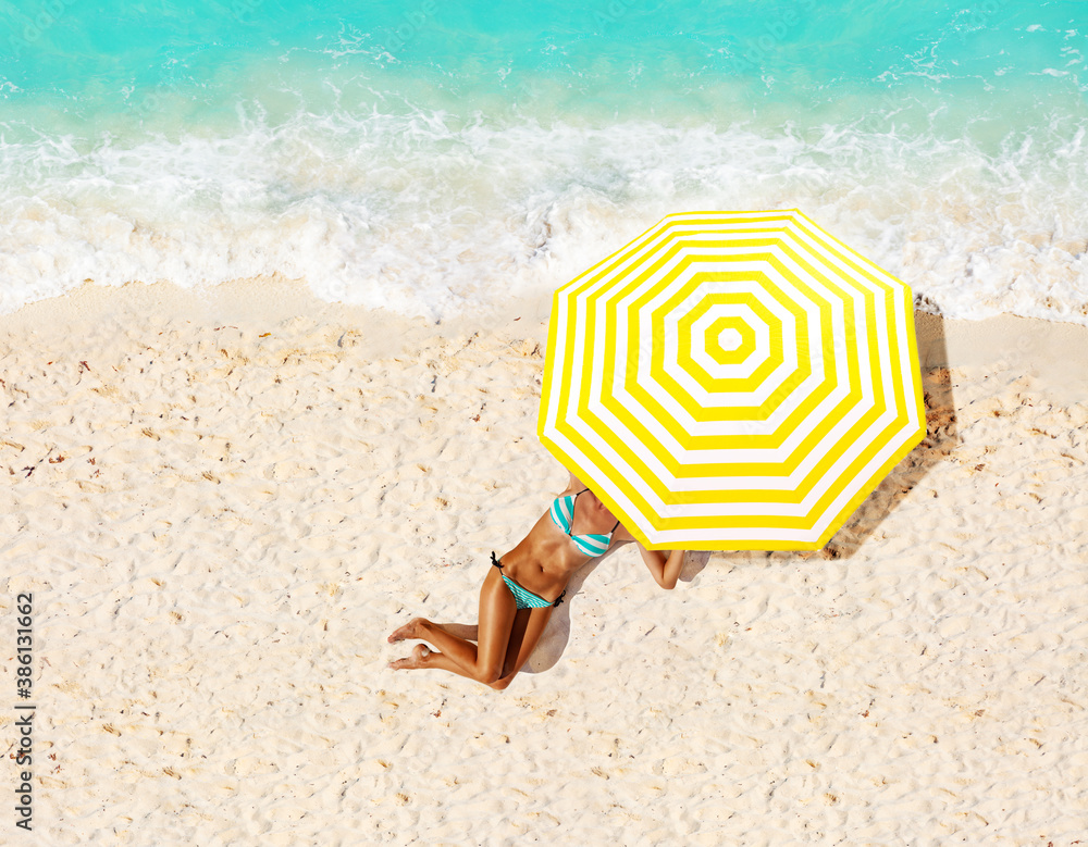 Woman on a beach under umbrella taking sun bath view from above near ocean waves