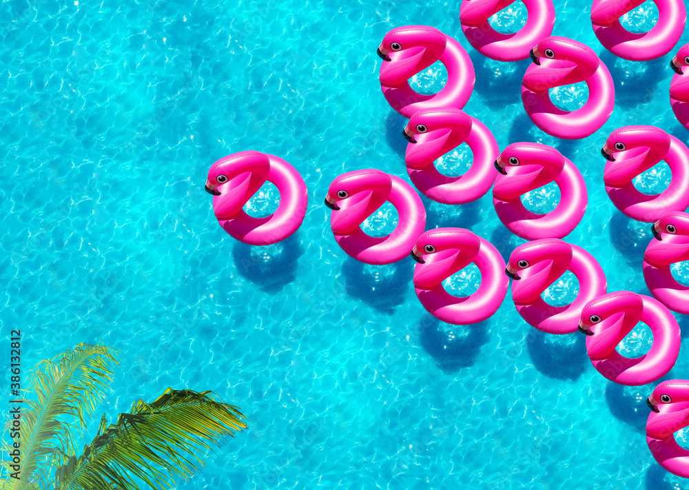 Large group of inflatable flamingo buoys swim in the swimming pool view from above under with palm t