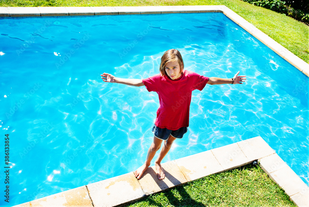 Happy boy stand on the border of the swimming pool stretching hands