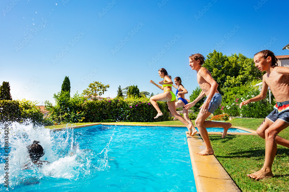 Group of happy teenage kids run into water pool jumping together view from side