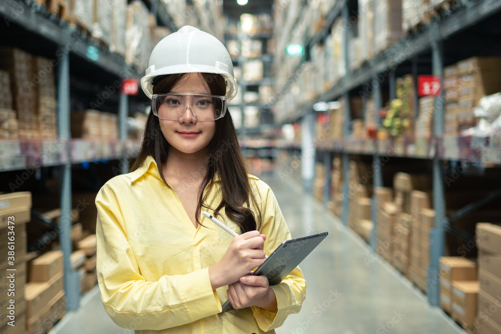 Female warehouse worker inspecting a warehouse in a factory. Wear a safety helmet and glasses for wo