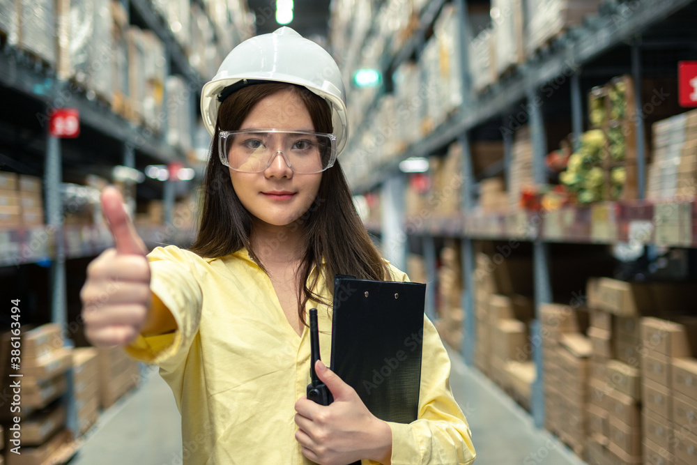 Female warehouse worker inspecting a warehouse in a factory. Wear a safety helmet and glasses for wo