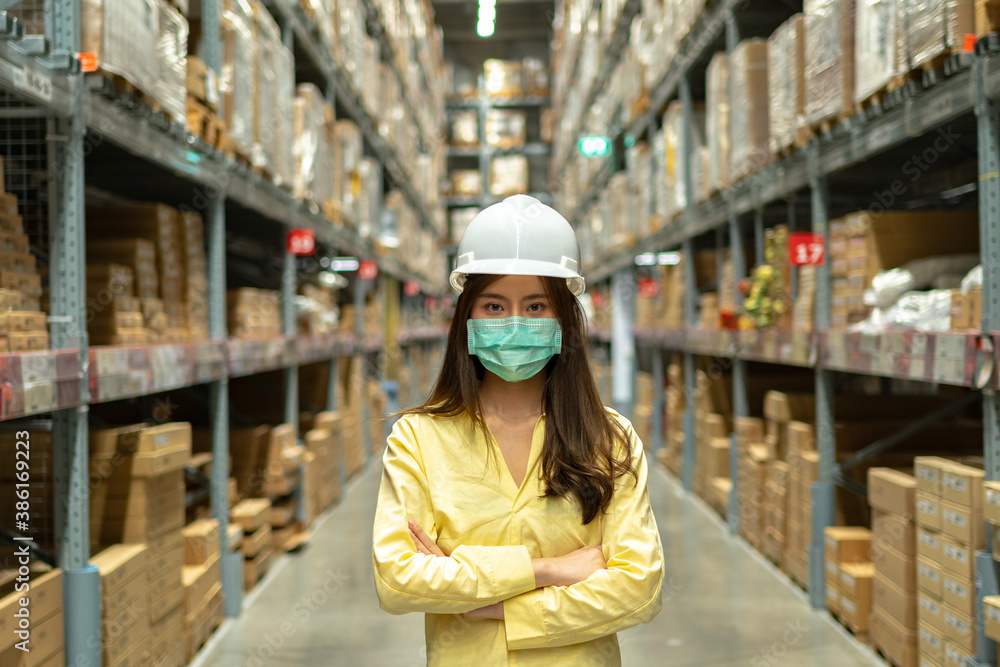 Female warehouse worker inspecting a warehouse in a factory. Wear a safety helmet and mask for worki