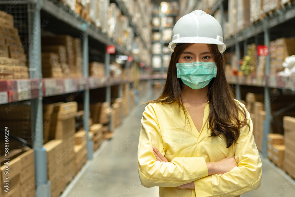 Female warehouse worker inspecting a warehouse in a factory. Wear a safety helmet and mask for worki