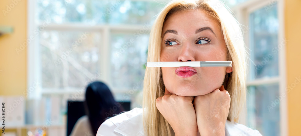 Young woman holding a pen above lips in an office