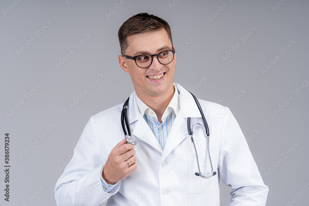 Portrait of doctor in scrubs. Gray background. Smiling doctor in glasses with phonendoscope. Close u