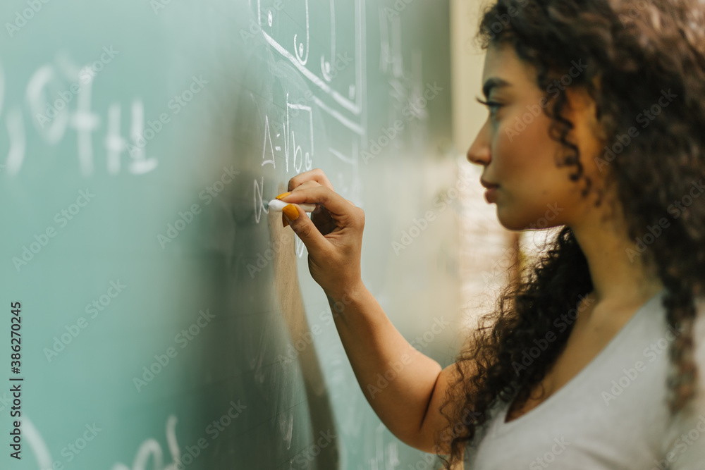 Latin student in the classroom. curly haired woman student writing assignments on blackboard during 