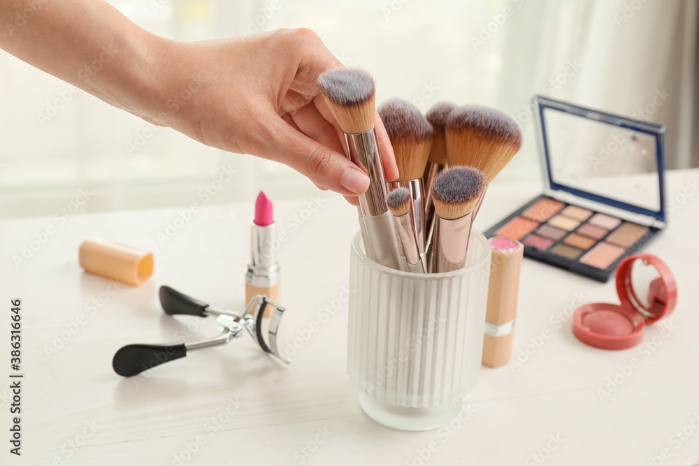 Woman taking makeup brush from dressing table